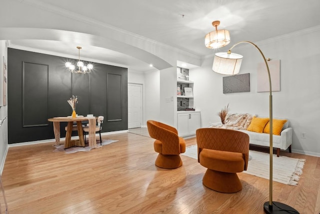 living area featuring light wood-type flooring, arched walkways, ornamental molding, and an inviting chandelier