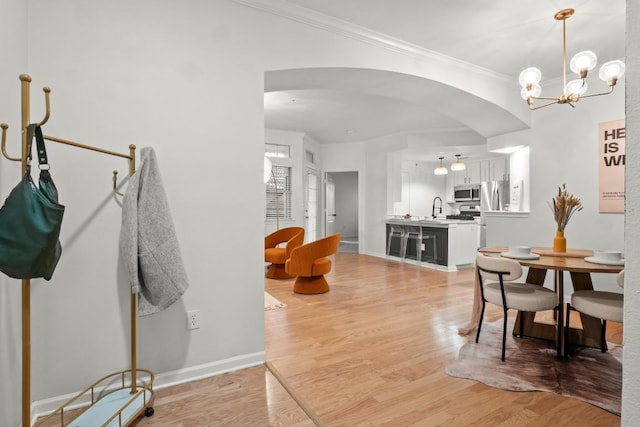 dining area featuring light wood-type flooring, baseboards, arched walkways, and ornamental molding