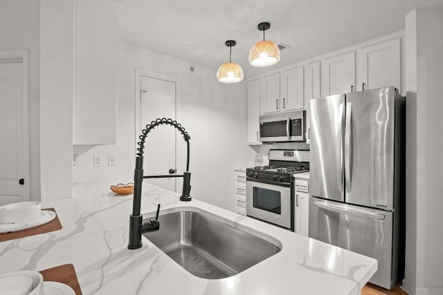 kitchen featuring stainless steel appliances, hanging light fixtures, a sink, and white cabinetry