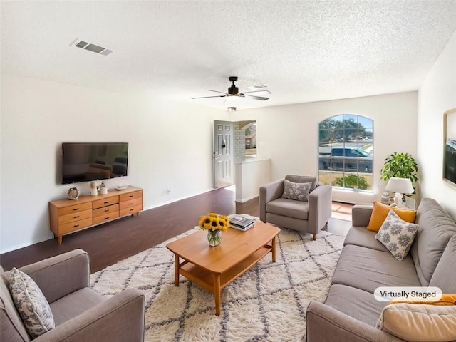 living area featuring a ceiling fan, light wood-type flooring, visible vents, and a textured ceiling