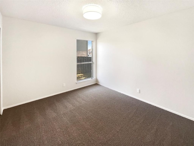 spare room with a textured ceiling, dark colored carpet, and baseboards