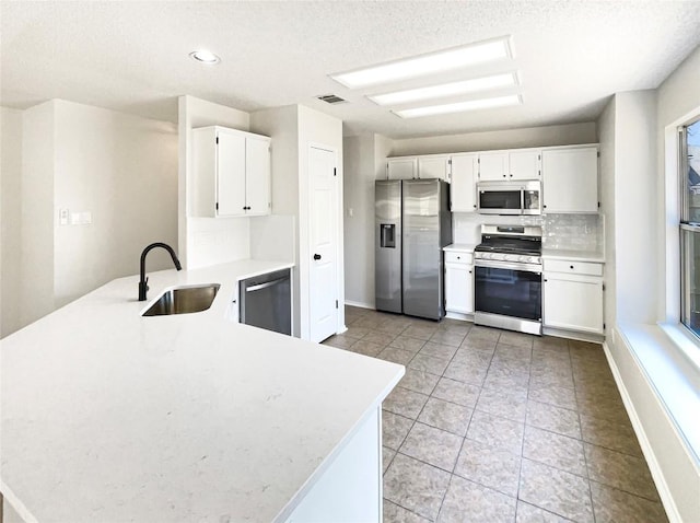 kitchen with stainless steel appliances, light countertops, decorative backsplash, a sink, and a peninsula