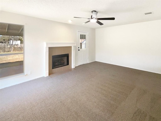 unfurnished living room featuring carpet, a textured ceiling, and a tile fireplace