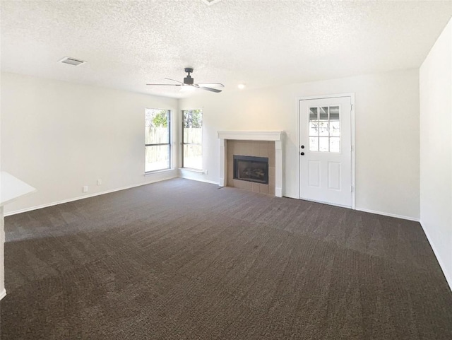 unfurnished living room featuring dark carpet, a ceiling fan, a textured ceiling, a tile fireplace, and baseboards