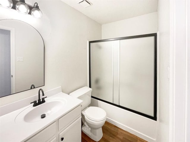 full bathroom with visible vents, bath / shower combo with glass door, toilet, wood finished floors, and vanity