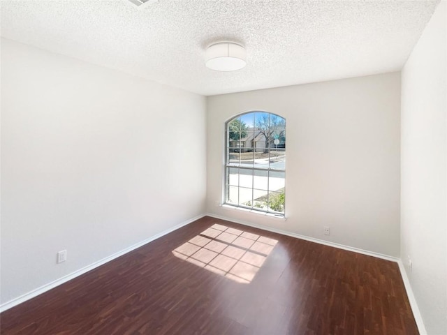 spare room featuring a textured ceiling, wood finished floors, and baseboards