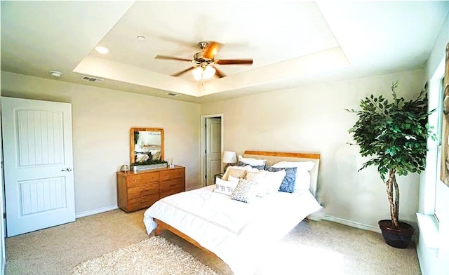 bedroom with light carpet, visible vents, baseboards, a ceiling fan, and a tray ceiling