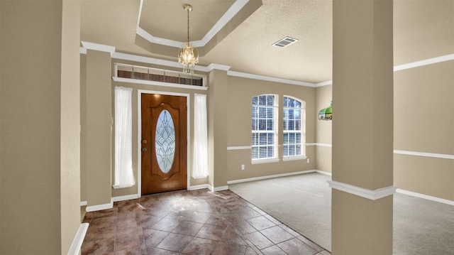 carpeted entrance foyer with baseboards, visible vents, a tray ceiling, crown molding, and a notable chandelier