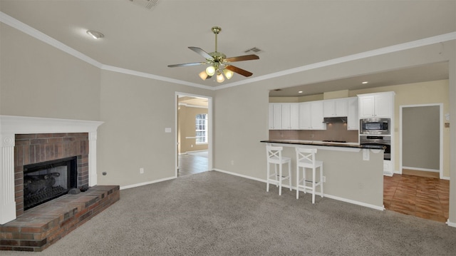 kitchen with stainless steel appliances, carpet floors, a brick fireplace, and under cabinet range hood