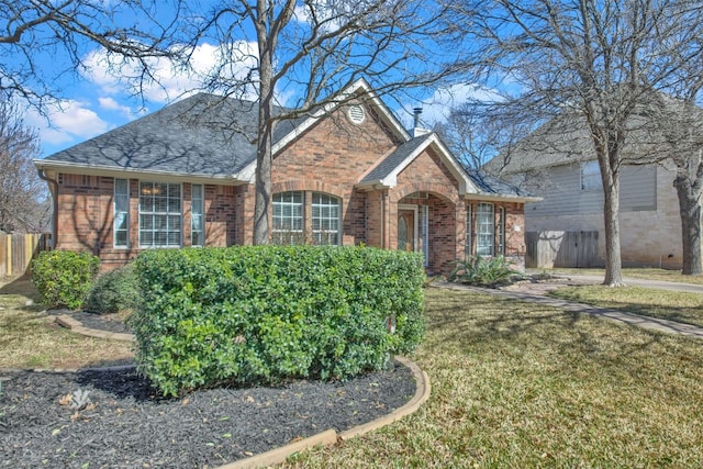 traditional home featuring a shingled roof, brick siding, fence, and a front lawn