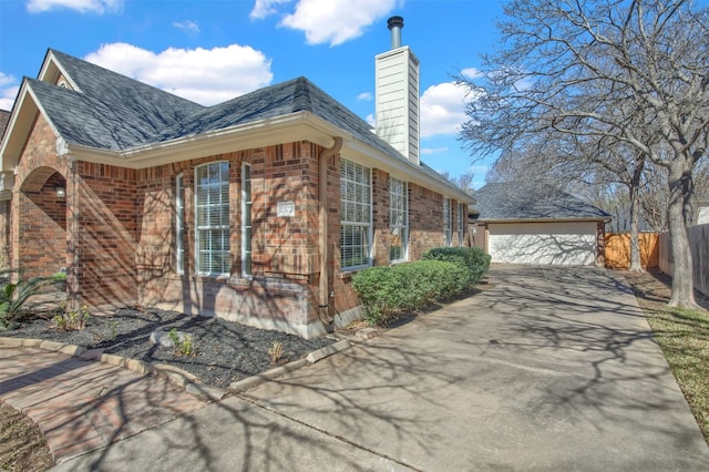 view of home's exterior featuring a chimney, fence, concrete driveway, brick siding, and a detached garage