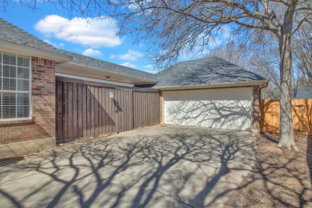 view of property exterior with a garage, concrete driveway, roof with shingles, fence, and brick siding