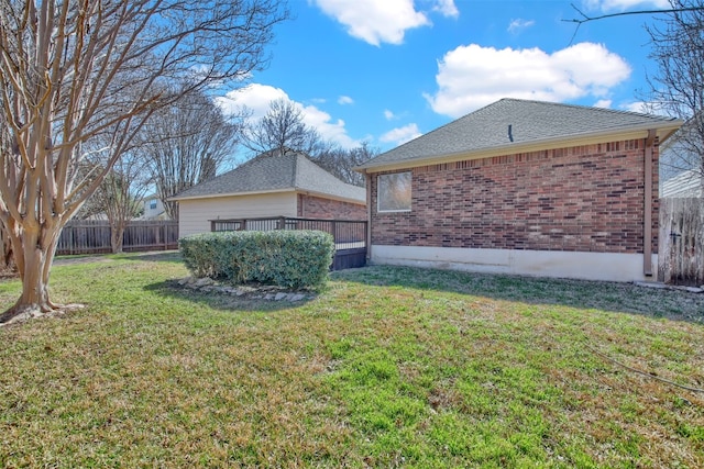 view of property exterior featuring a yard, a shingled roof, fence, and brick siding