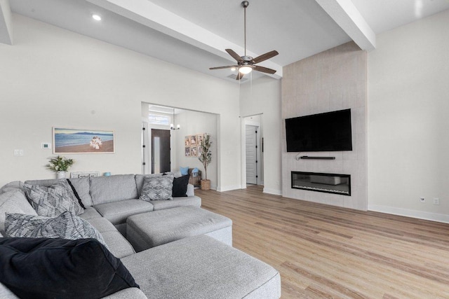 living area with baseboards, a ceiling fan, light wood-type flooring, a fireplace, and beam ceiling