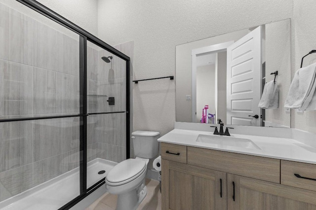 bathroom with toilet, a textured wall, a shower stall, and vanity