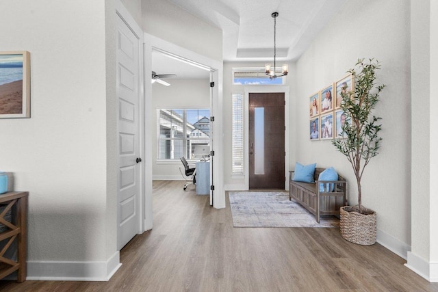 foyer featuring an inviting chandelier, a raised ceiling, baseboards, and wood finished floors