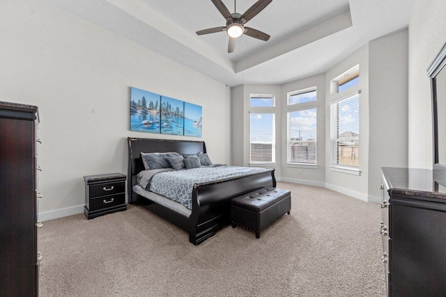 bedroom featuring a tray ceiling, light carpet, ceiling fan, and baseboards