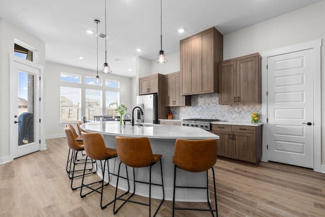 kitchen featuring a center island with sink, stainless steel refrigerator with ice dispenser, backsplash, light wood-style floors, and a kitchen breakfast bar