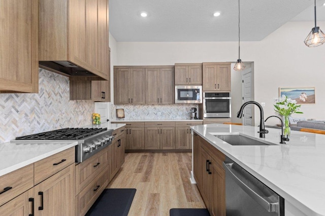 kitchen featuring appliances with stainless steel finishes, light wood-style floors, premium range hood, pendant lighting, and a sink