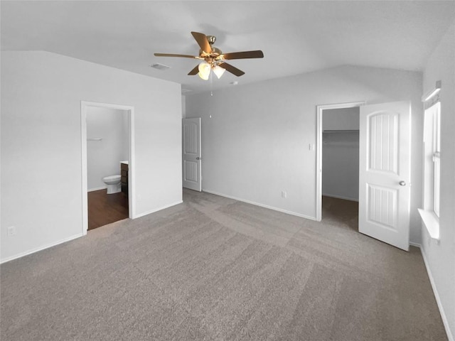 unfurnished bedroom with a walk in closet, a closet, visible vents, vaulted ceiling, and connected bathroom