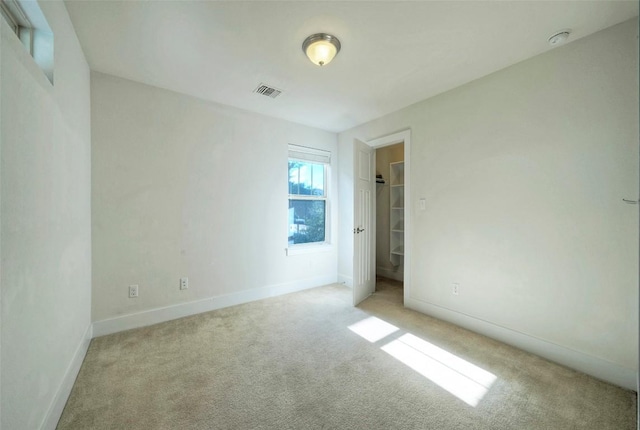 unfurnished bedroom featuring a walk in closet, a closet, light colored carpet, visible vents, and baseboards