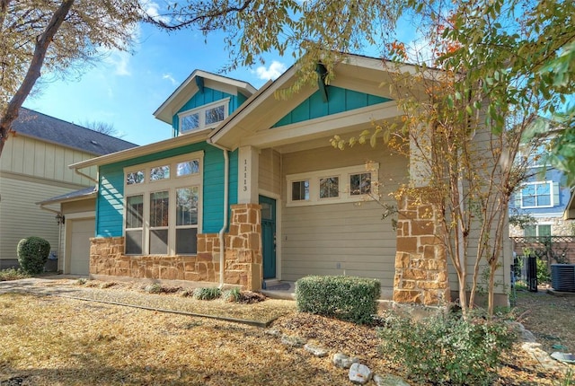 view of front of property with board and batten siding, stone siding, a garage, and central air condition unit