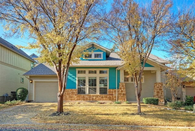 view of front facade featuring a garage, stone siding, a shingled roof, and gravel driveway