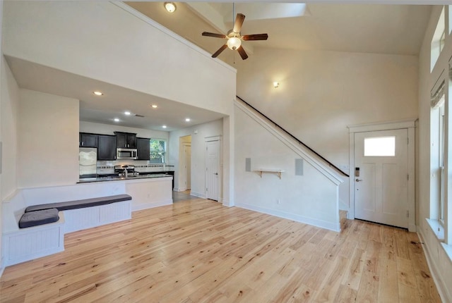 unfurnished living room with recessed lighting, high vaulted ceiling, light wood-type flooring, baseboards, and stairs