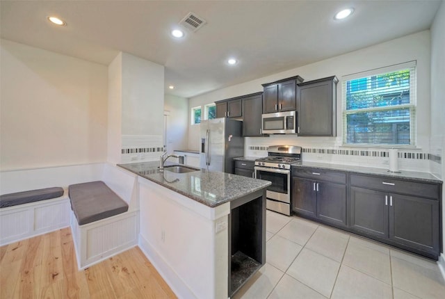 kitchen featuring visible vents, light stone counters, a peninsula, stainless steel appliances, and a sink