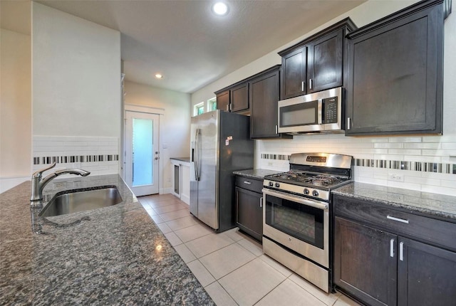 kitchen with decorative backsplash, appliances with stainless steel finishes, light tile patterned flooring, a sink, and dark stone counters