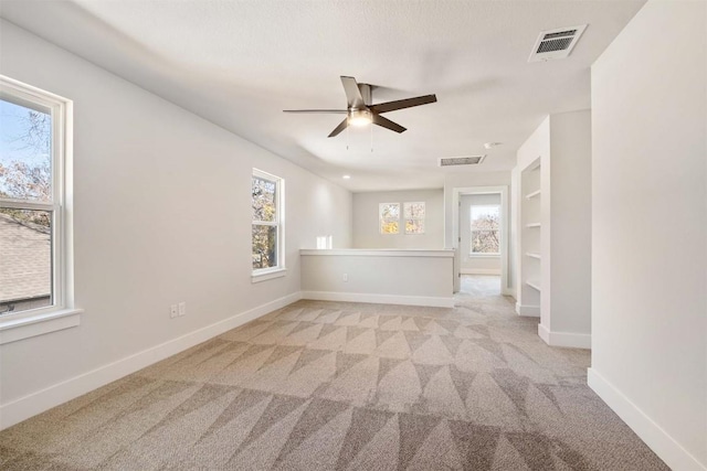 unfurnished room with built in features, light colored carpet, visible vents, and baseboards