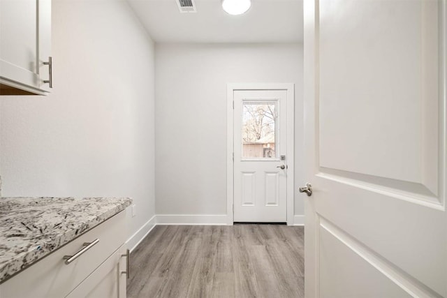 doorway with light wood finished floors, baseboards, and visible vents