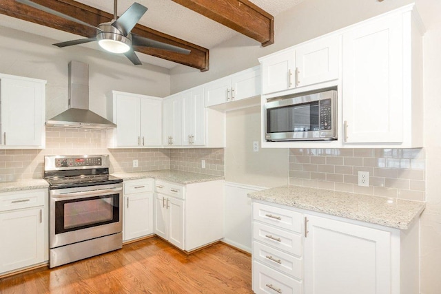 kitchen featuring beam ceiling, light wood finished floors, appliances with stainless steel finishes, white cabinets, and wall chimney range hood