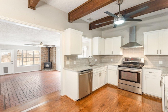 kitchen with a sink, white cabinetry, wall chimney range hood, appliances with stainless steel finishes, and backsplash