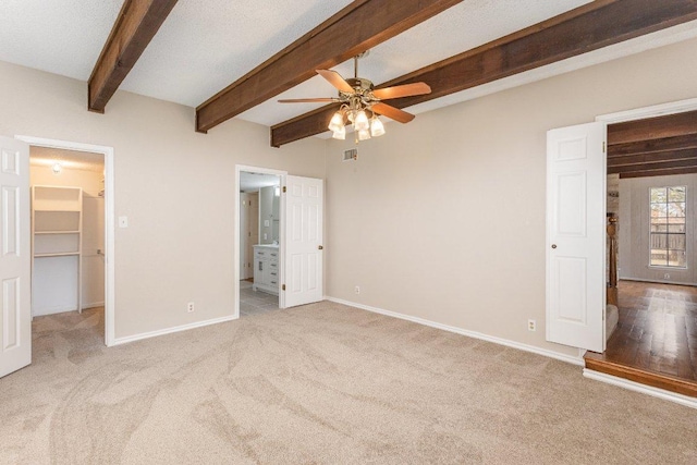 unfurnished bedroom with beam ceiling, baseboards, a walk in closet, and carpet flooring