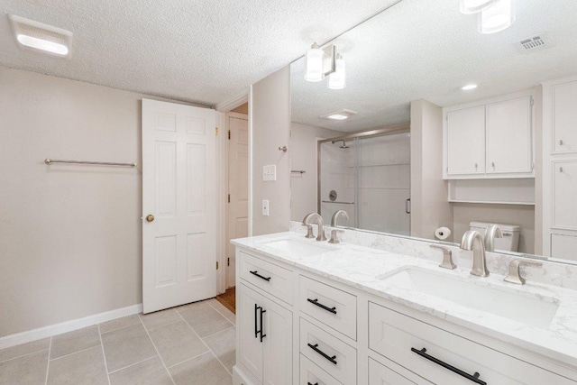 full bath with a sink, a shower stall, a textured ceiling, and double vanity