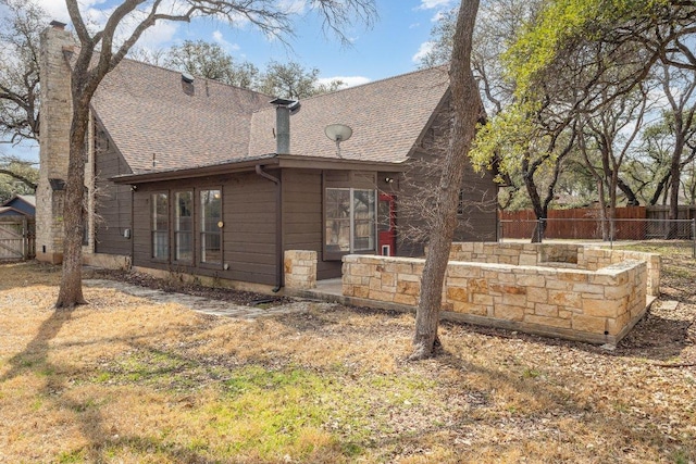 view of side of property featuring a patio, stone siding, a chimney, roof with shingles, and fence