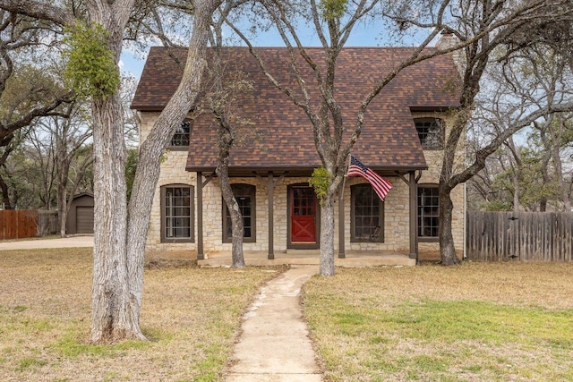 view of front of home featuring stone siding, a shingled roof, fence, and covered porch