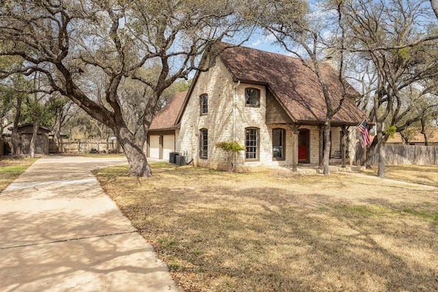 view of front of home with stone siding, central AC, fence, and driveway