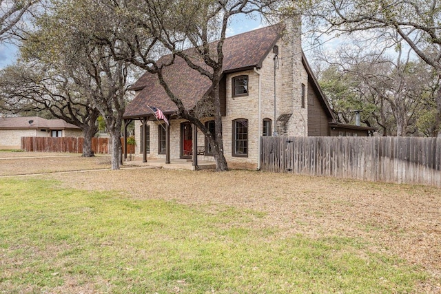 view of front of house with a front yard, stone siding, roof with shingles, and fence