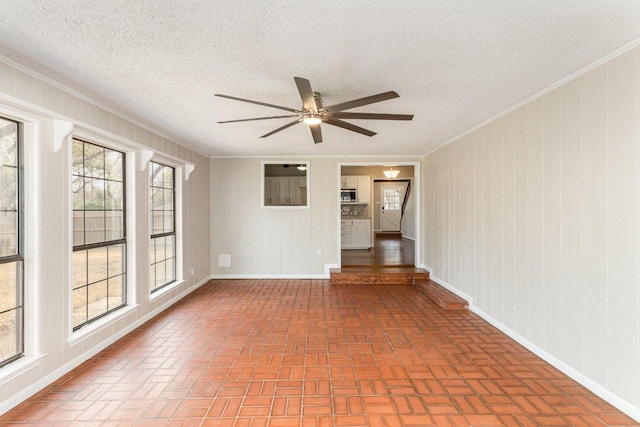 spare room with baseboards, ceiling fan, brick floor, a textured ceiling, and crown molding