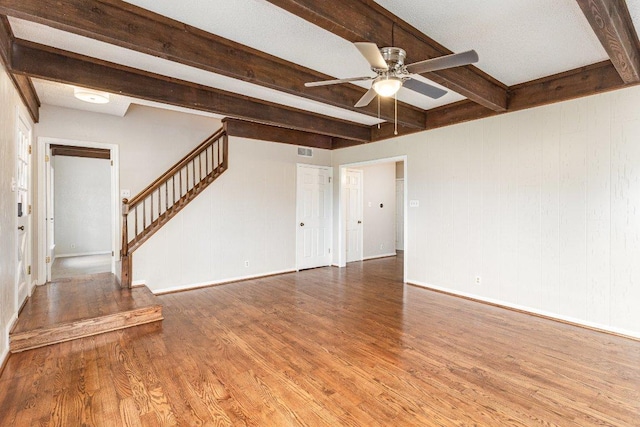 unfurnished living room with wood finished floors, a ceiling fan, baseboards, stairs, and beam ceiling