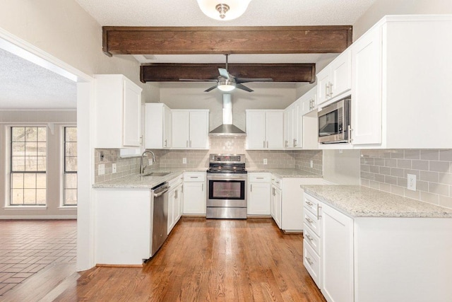 kitchen featuring stainless steel appliances, a sink, wall chimney range hood, a textured ceiling, and light stone countertops