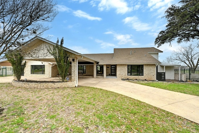 exterior space with a shingled roof, brick siding, fence, concrete driveway, and a front lawn