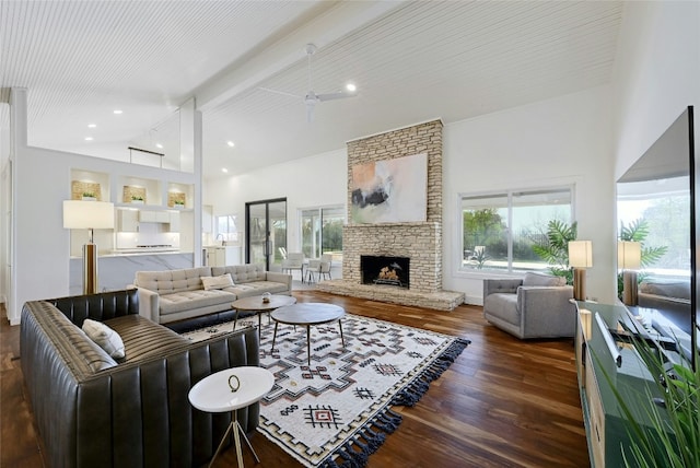 living room with beamed ceiling, a stone fireplace, dark wood-style flooring, and a wealth of natural light