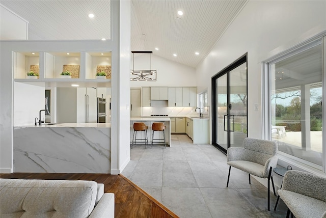 interior space featuring a kitchen bar, high vaulted ceiling, light countertops, and a sink