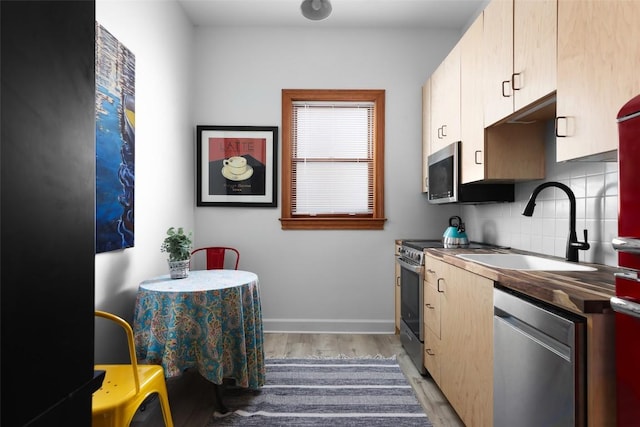 kitchen with light wood-style flooring, stainless steel appliances, a sink, backsplash, and dark countertops