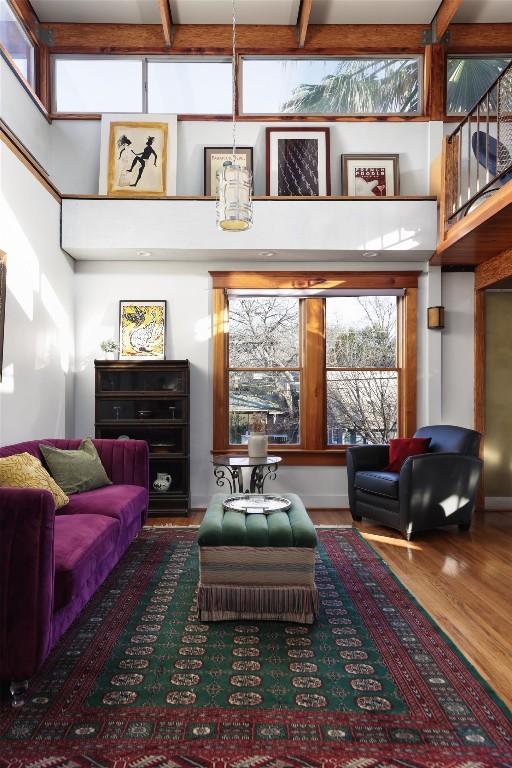 living area with beamed ceiling, wood finished floors, and a towering ceiling