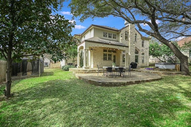 back of house featuring fence, a lawn, stucco siding, a patio area, and a hot tub