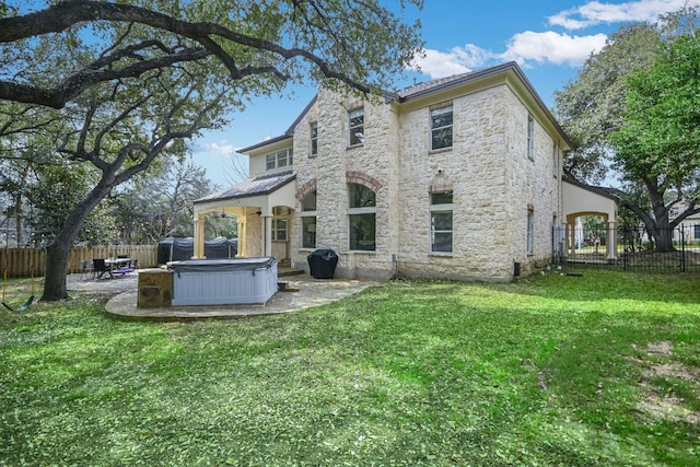 rear view of property with stone siding, a patio area, a fenced backyard, and a hot tub